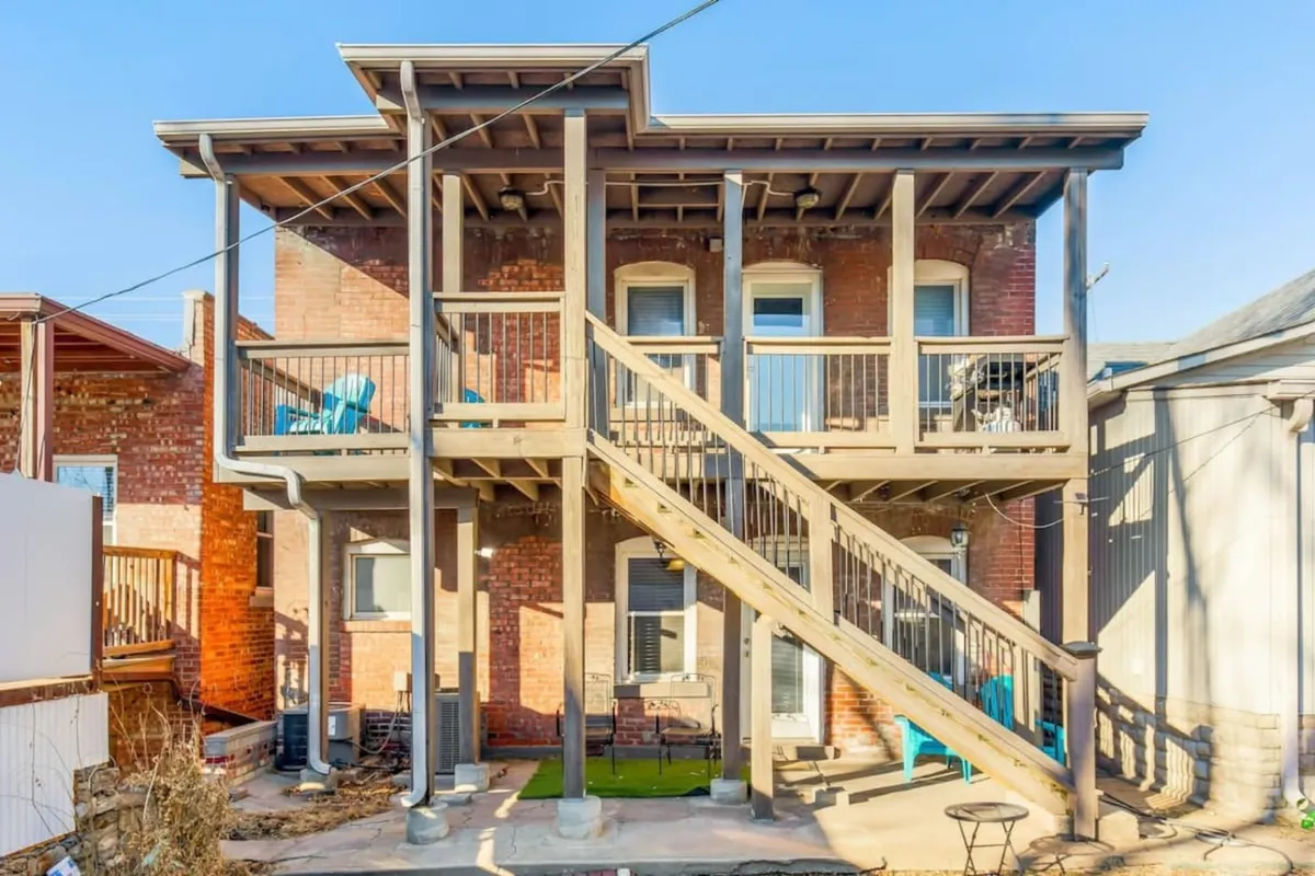 A spacious outdoor area with a wooden staircase, balconies furnished with chairs, and a classic brick facade. The scene invites guests to enjoy outdoor relaxation, conversation, or city views from the comfort of home.