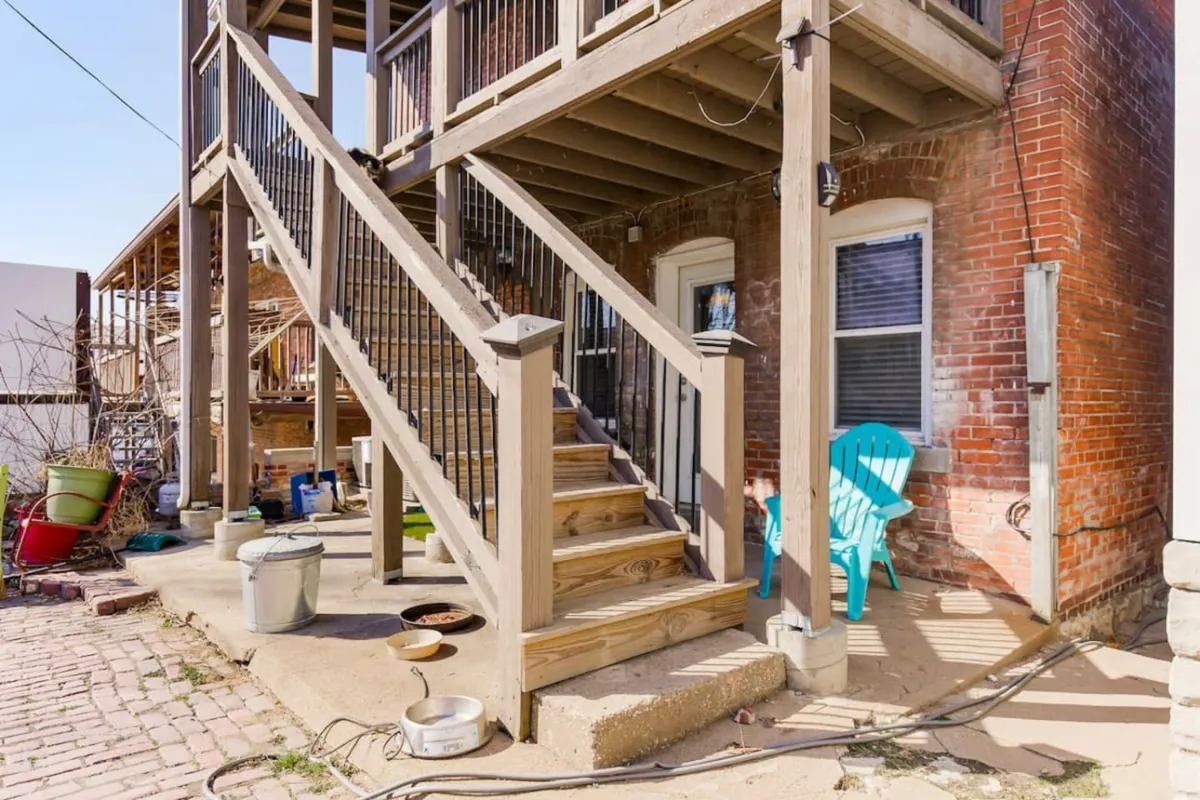 The image shows wooden stairs and a blue chair set against a brick wall in an exterior area. The inviting outdoor setting hints at opportunities to relax with a cup of coffee or enjoy meals outside, reinforcing the residential nature of the property.